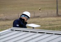 Worker inspecting Amazon Leo antenna mounted on a building roof